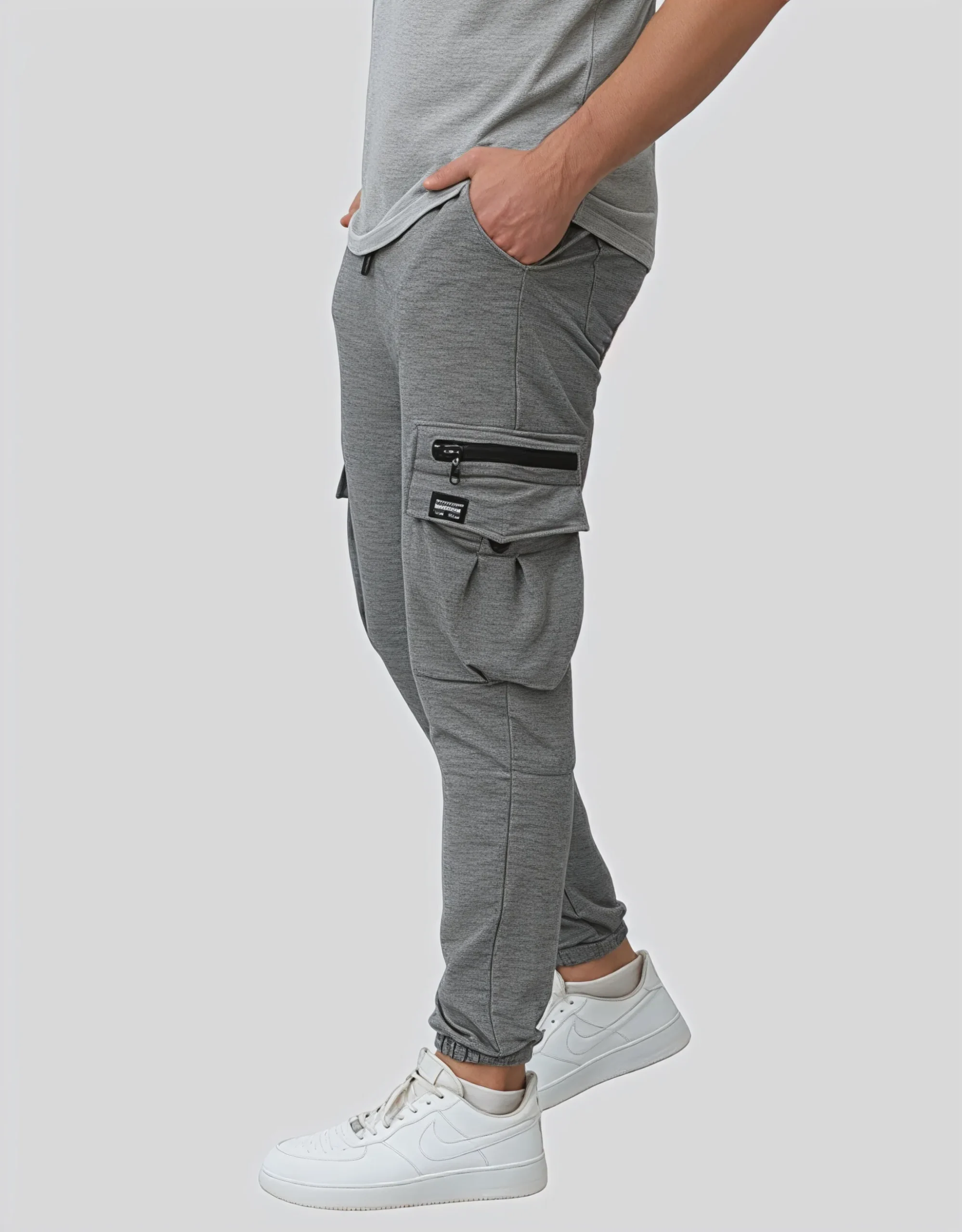 Men's gray cargo jogger pants worn on model left side view showing black zipper hardware and elasticated ribbed ankle cuff