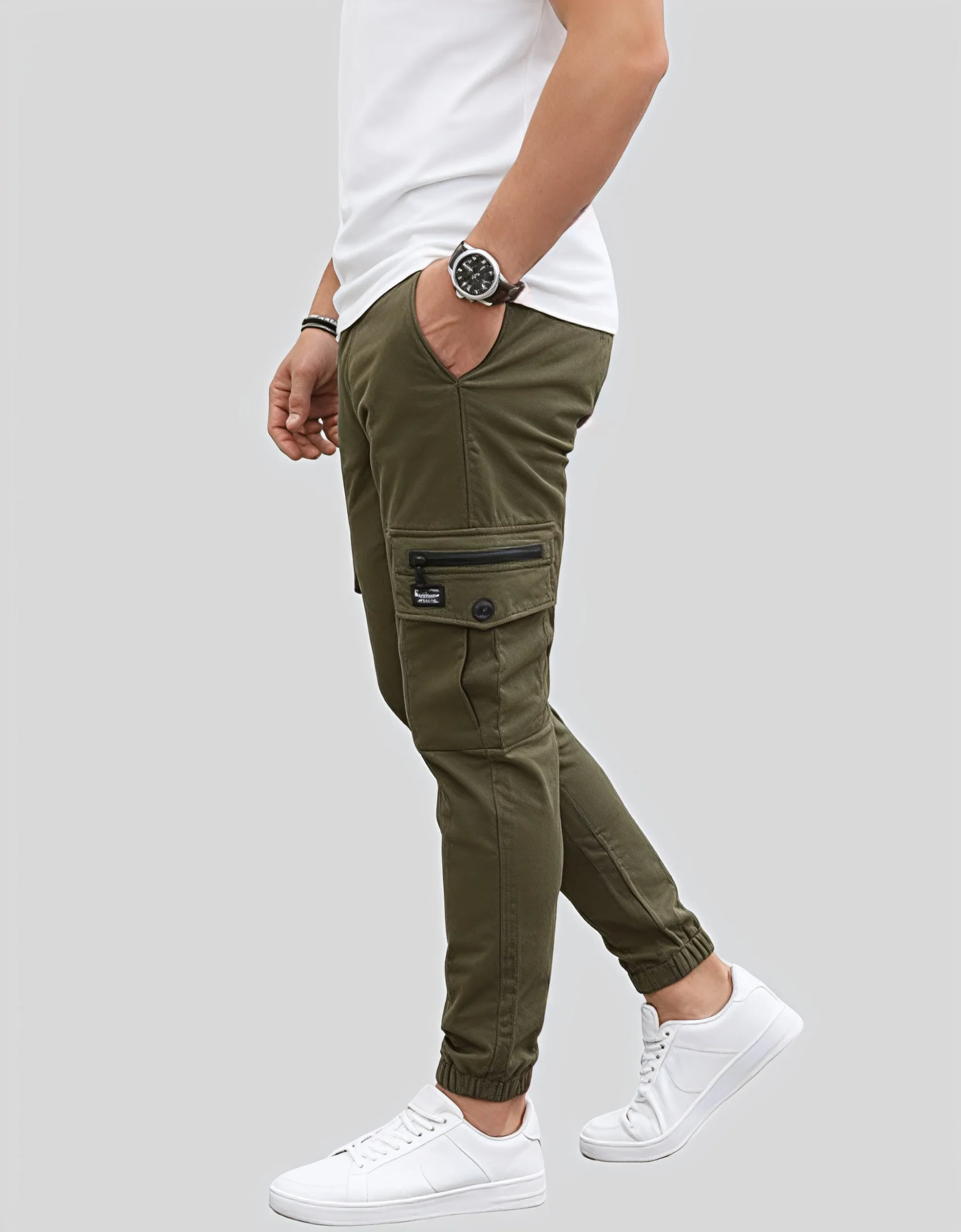 Men's military green cargo jogger pants worn on model left side view showing black zippered cargo pocket with button closure and brand label patch