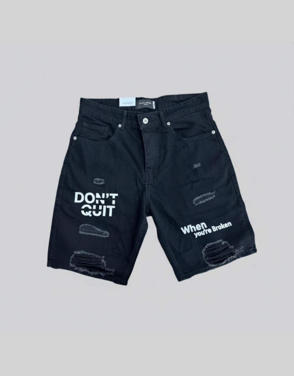 Flat lay of men's dark blue distressed denim shorts with motivational slogan screen print